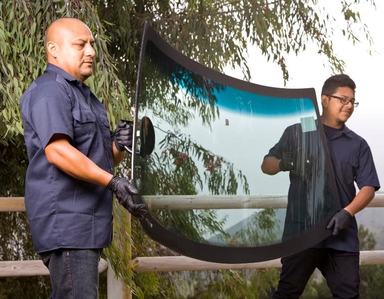 Two men lifting a windshield that needs to be installed for a car in Miami, FL